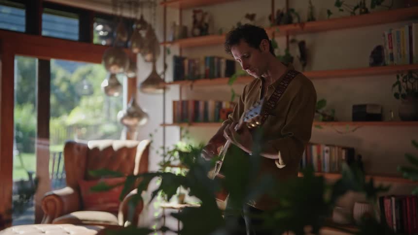 A man playing an acoustic guitar inside a room in a house