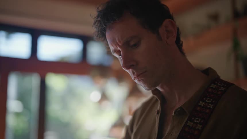 Man in a dress shirt with a button nodding his head slightly