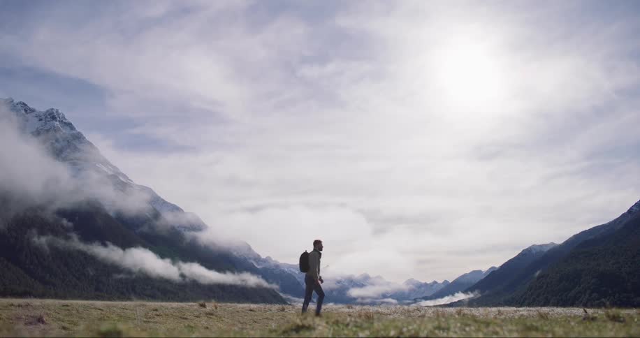 Man with backpack on back walking around mountains