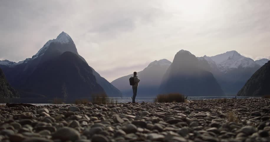A man standing on the edge of a river and looking ahead thinking