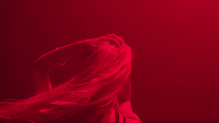 Blonde woman from the back dancing at a club under red lights