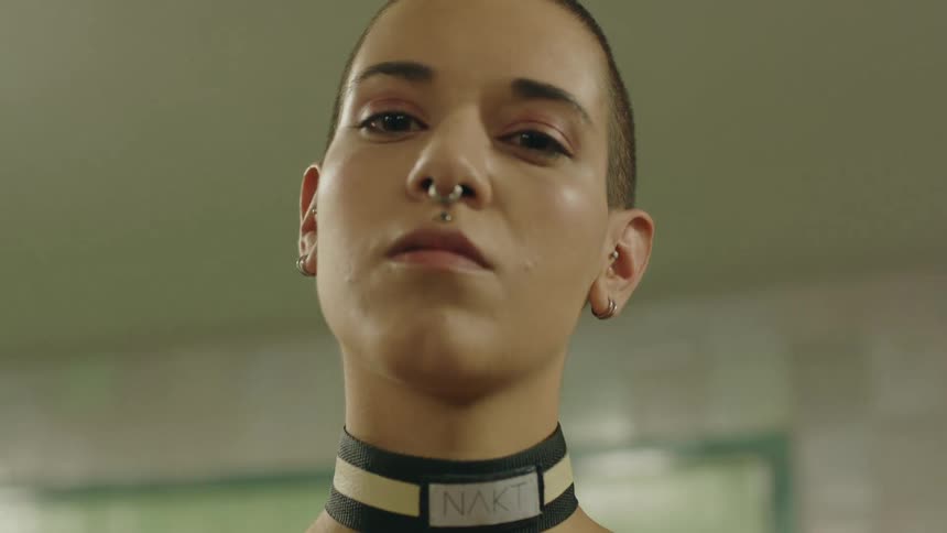 A woman wearing a nose ring and neck belt with very short hair looking flirtishly