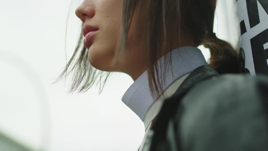 A woman is leaning against a pole outside