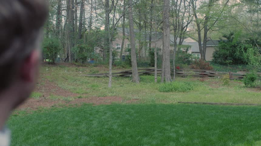 A man stands in front of a house surrounded by trees