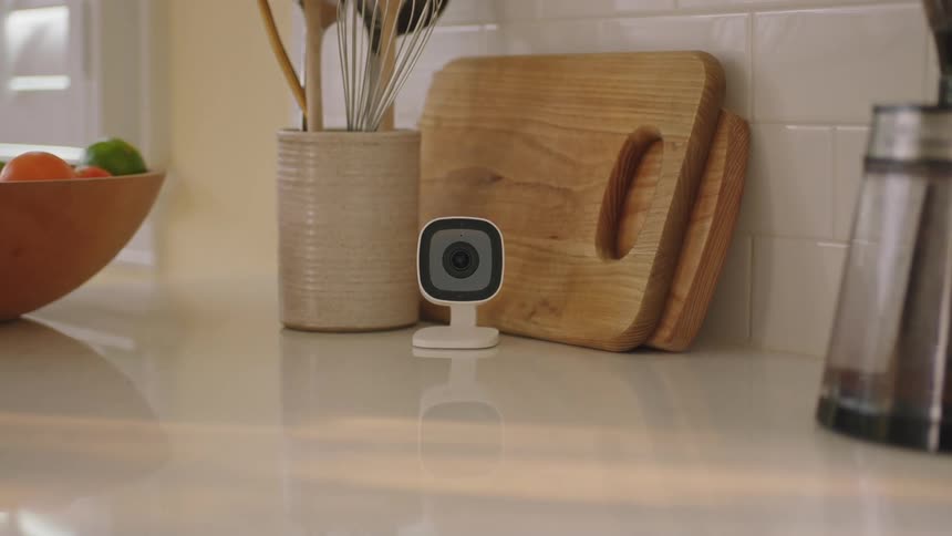 Small white camera on top of a table surrounded by kitchen equipment and fruits