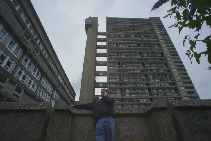 Person talking on the phone in an outdoor space with a massive residential building in the background