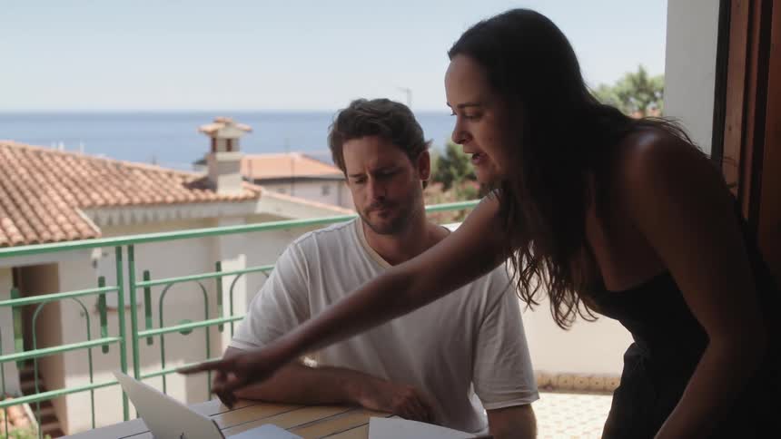 A man and woman are talking and using a laptop on the balcony