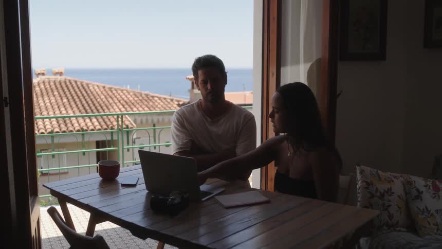 A man and a woman sitting at the table talking and working with a laptop in front of them