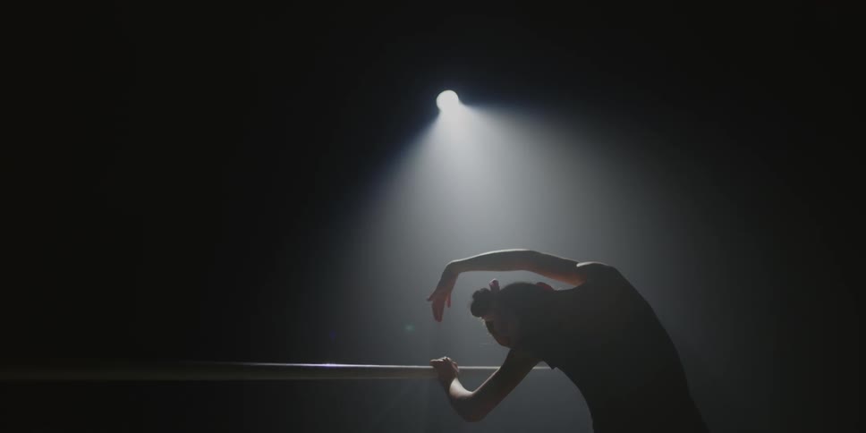 Female dancer stretching on a handrail under stage lights indoors