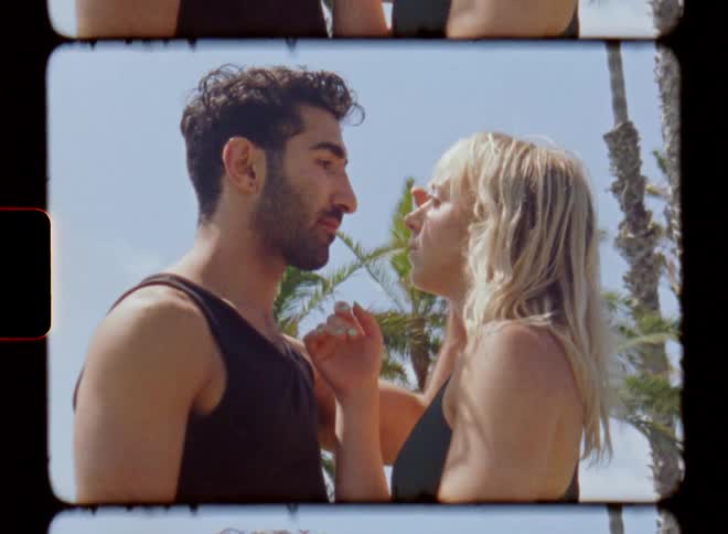 Man and woman gaze into each others eyes and caress face standing near palm trees