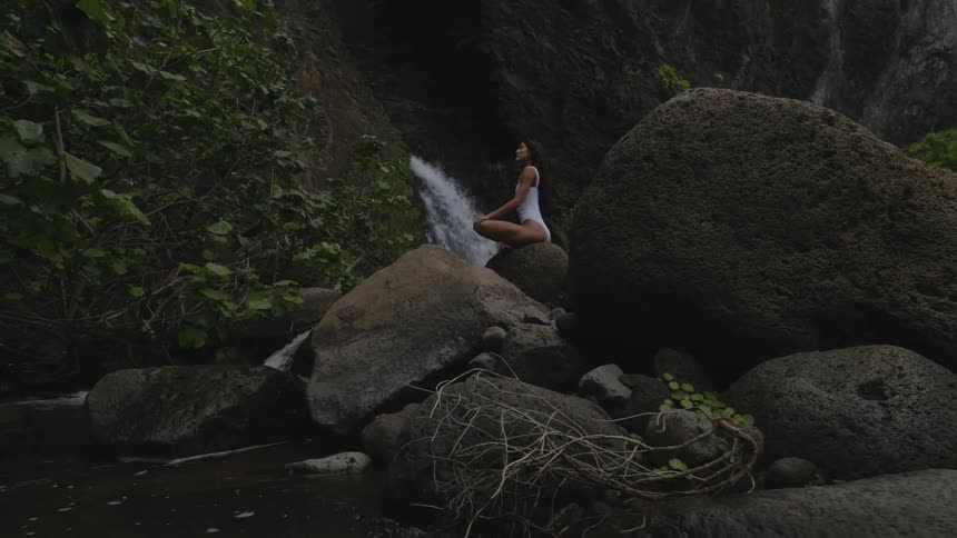 A woman is sitting on a boulder by the stream