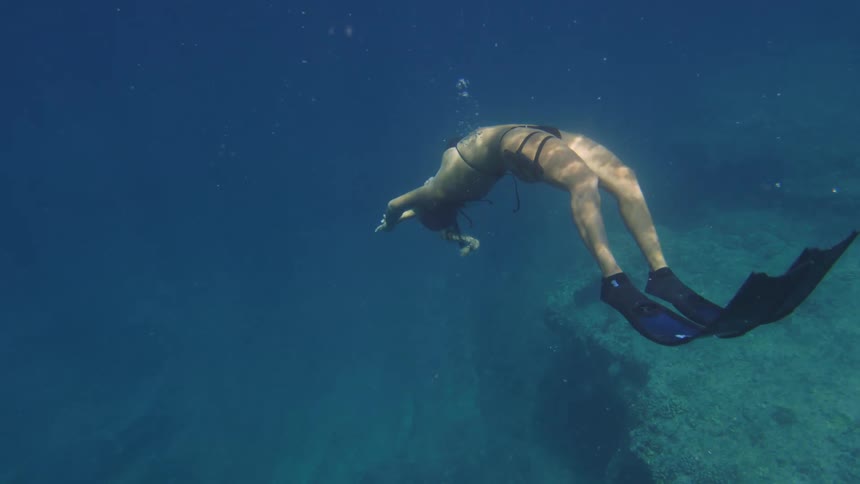 A woman in a bikini and fins swimming in the depths of the ocean
