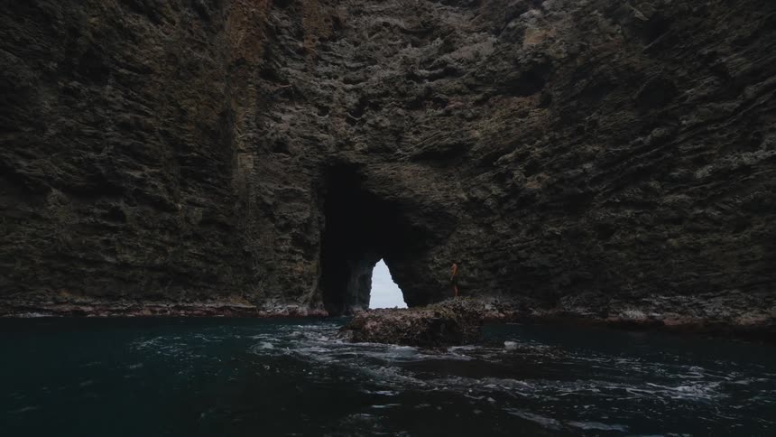 A man stands on top of a rock in the middle of the sea