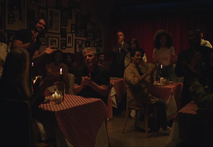 Several people sitting at tables in restaurants suddenly start clapping and standing up to applaud something or someone