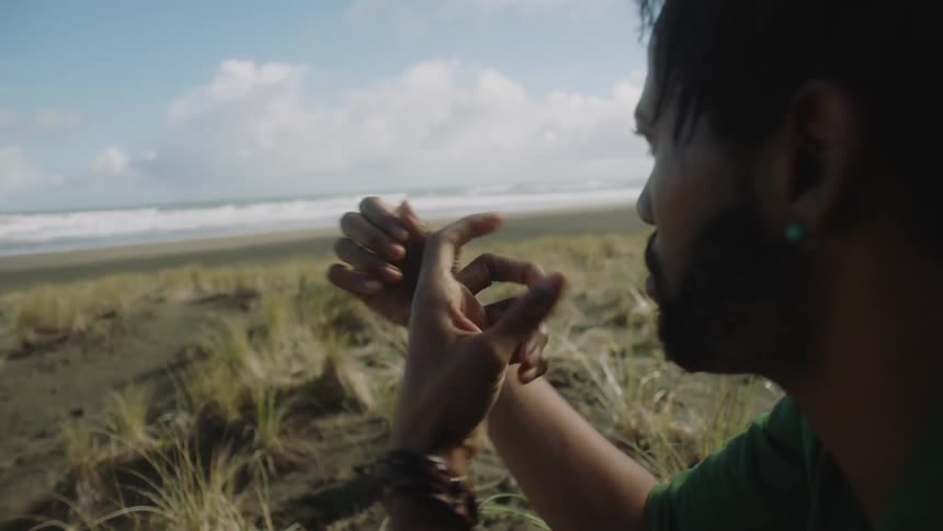 A black man at the shore on the grass doing acrobatic with his fingers in mid air