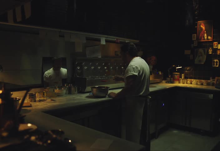 A man wearing a cooking apron standing at his kitchen counter as he prepares food and sauce out of a bowl