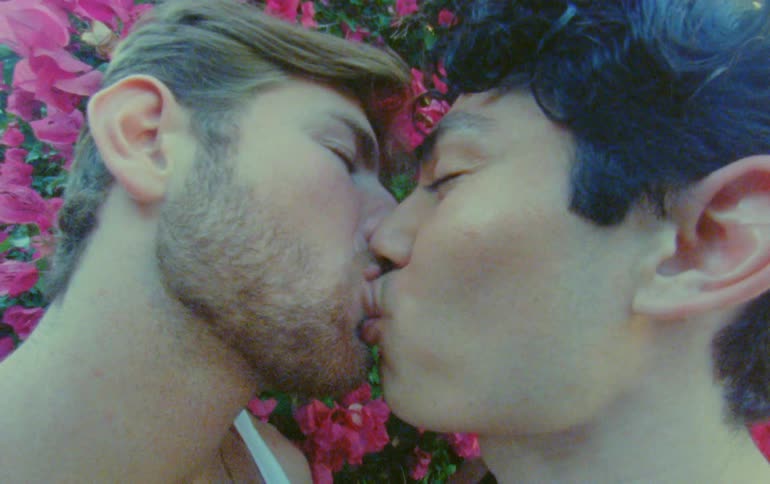 Male couple smiles while kissing near flowering bush
