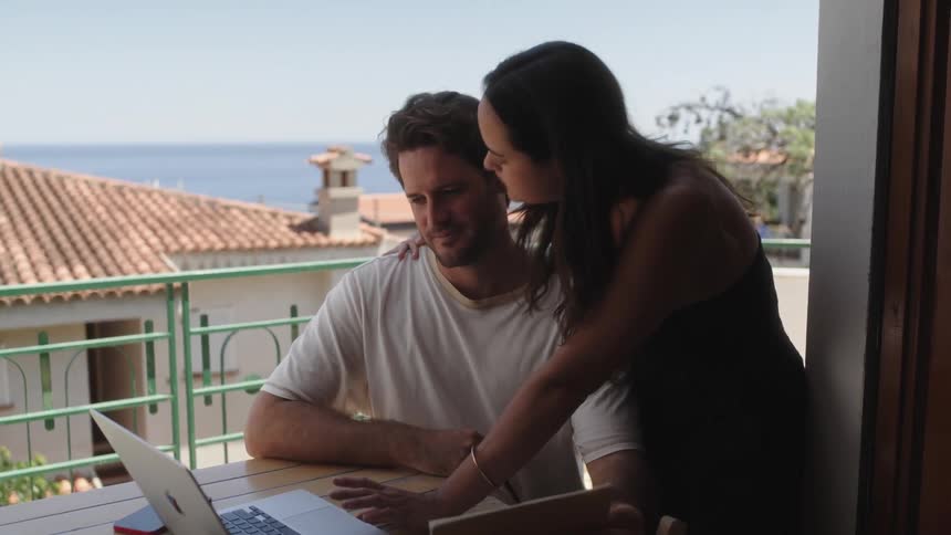 A woman and a man are sitting at a table typing on a computer