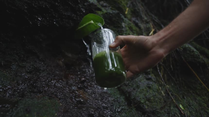 Man fills a glass of green tea with water from a waterfall
