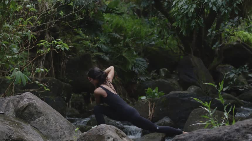 Woman wearing a black bodysuit doing yoga outdoors in a forest during day time