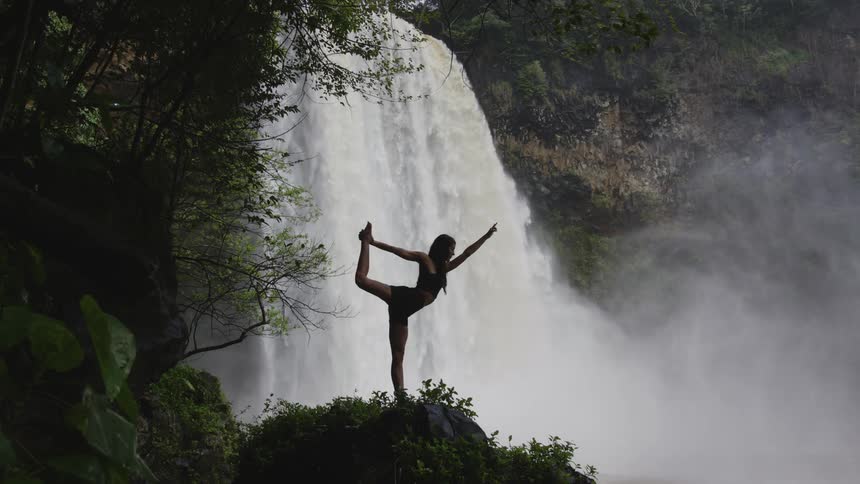 Woman stretches on a yoga pose in front of a waterfall