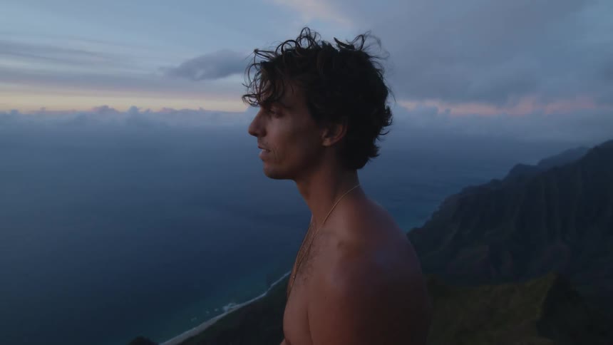 A young man on a mountain without a shirt observing the nature of the sky and sea