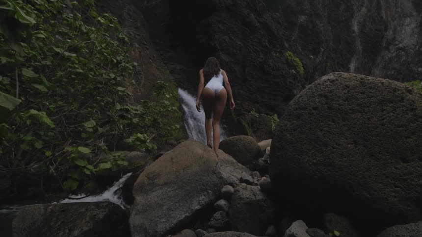 A woman walks on the rocks of a waterfall