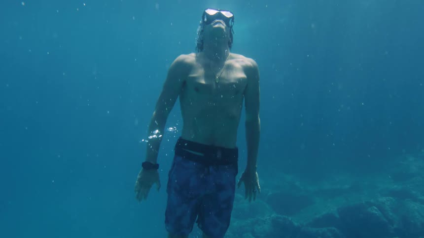A man submerged in the ocean diving towards the surface