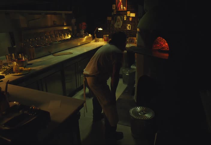 Man looks into a pizza oven turns and sits on stool