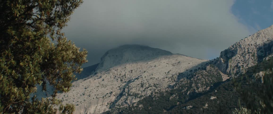 A storm approaches a mountain area at midday with trees nearby