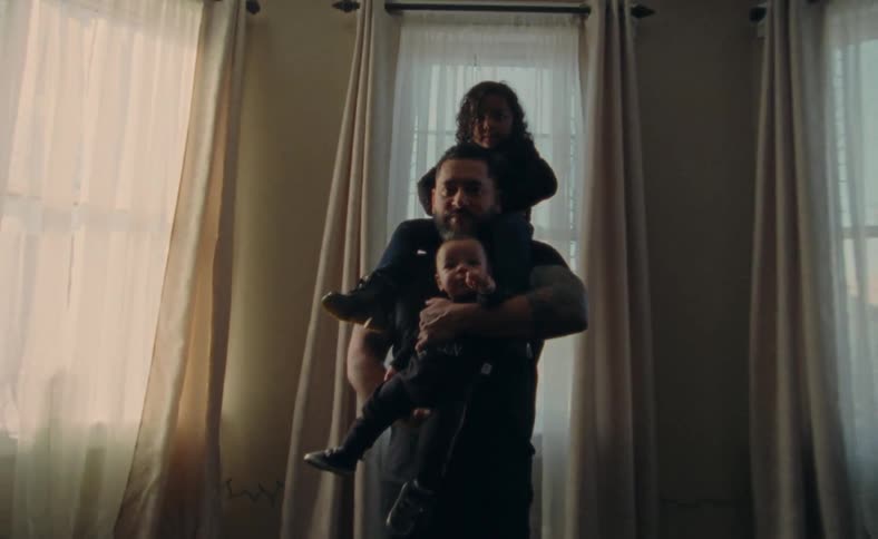 A man holding up a baby while a toddler rides on his shoulders
