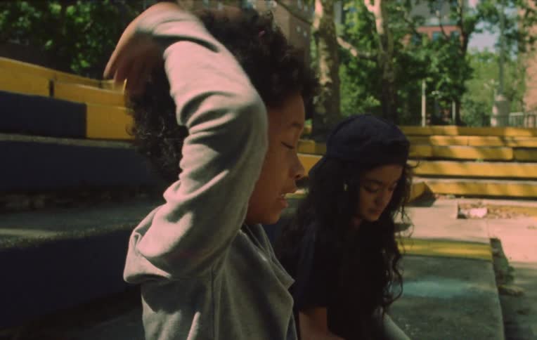 Two children sitting on a staircase in an open area and one of them tossing leaves up playing