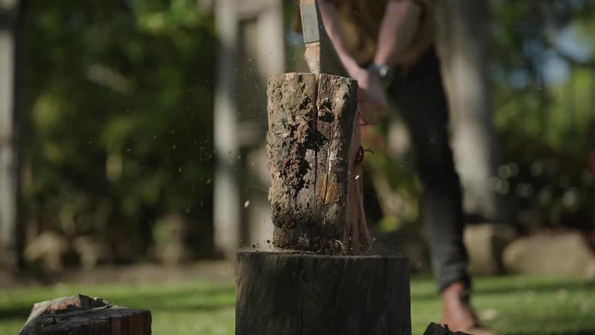 A man chops wood with an axe in a yard