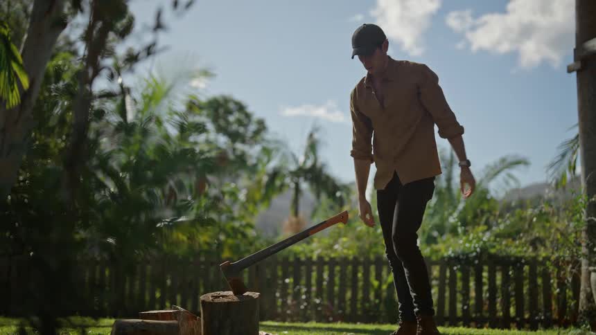 A man chops wood in a yard on a sunny day