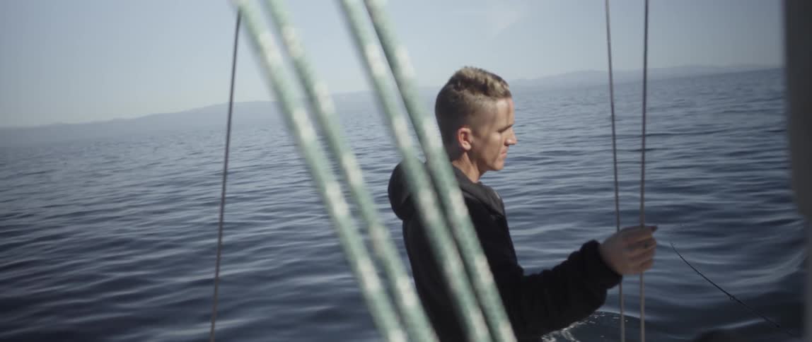 A man holds onto a rope as he stands on the ship