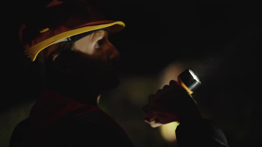 A man in a dark location wearing protective gear using a flashlight to inspect his surroundings