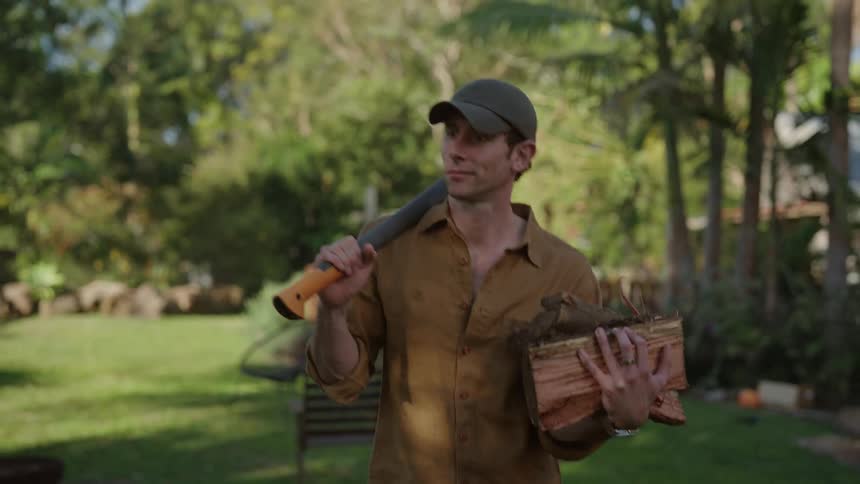 Man carries and axe and chopped wood through the backyard