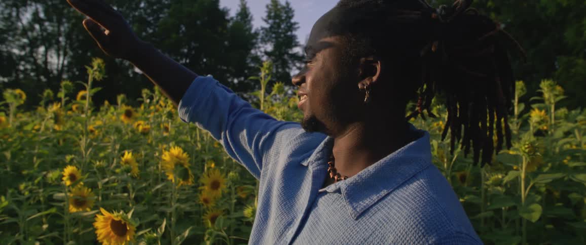 Man covers his eyes from the sun in a field of sunflowers at morning