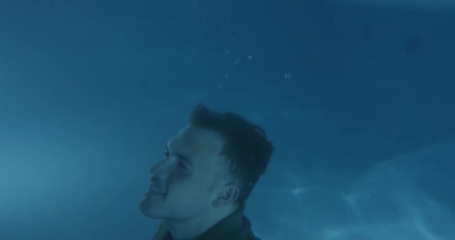 Fully clothed man submerges on a swimming pool at night