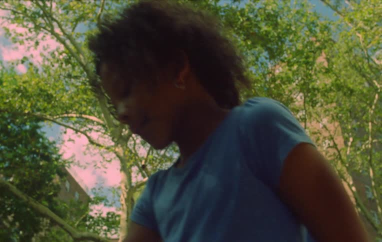 A black kid playing with a toy outdoor in an area filled with trees in the city