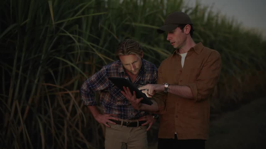 Two men stand outdoors talking pointing holding a tablet