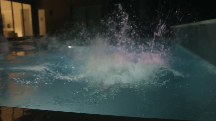 Two people jump into the pool at night
