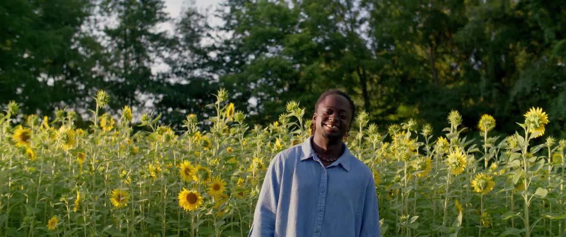 A woman looking ahead and breaking into a big smile in an environment filled with many sunflower flowers