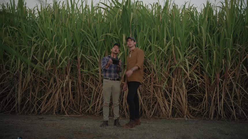 Two men in an outdoor agricultural setting with one of them holding a remote control and the other pointing to the sky giving instructions