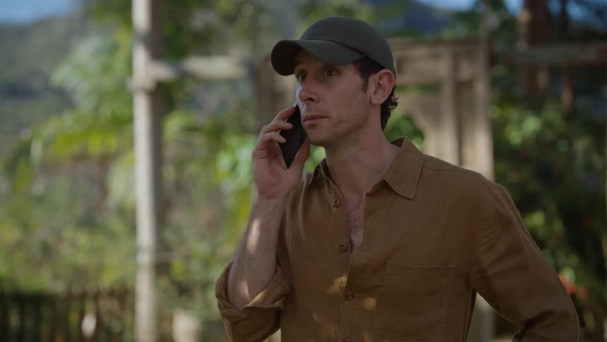A man talking on the phone and smiling in front of a park entrance