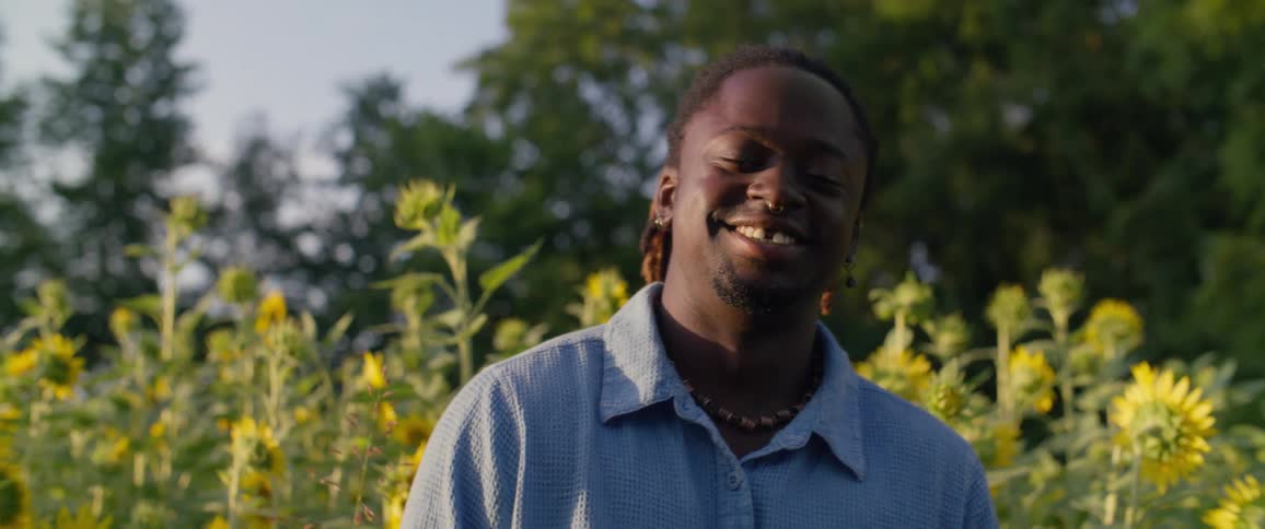 A black man smiles in a garden of sunflowers
