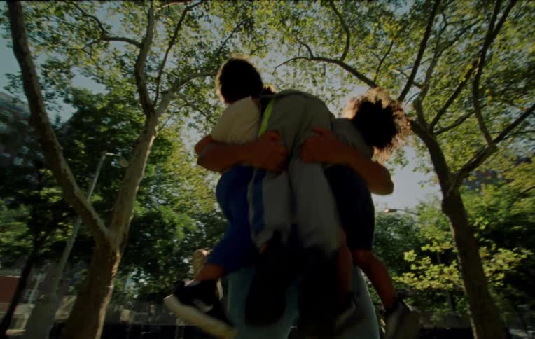 A father squats down and picks up three children outdoors on a sunny day