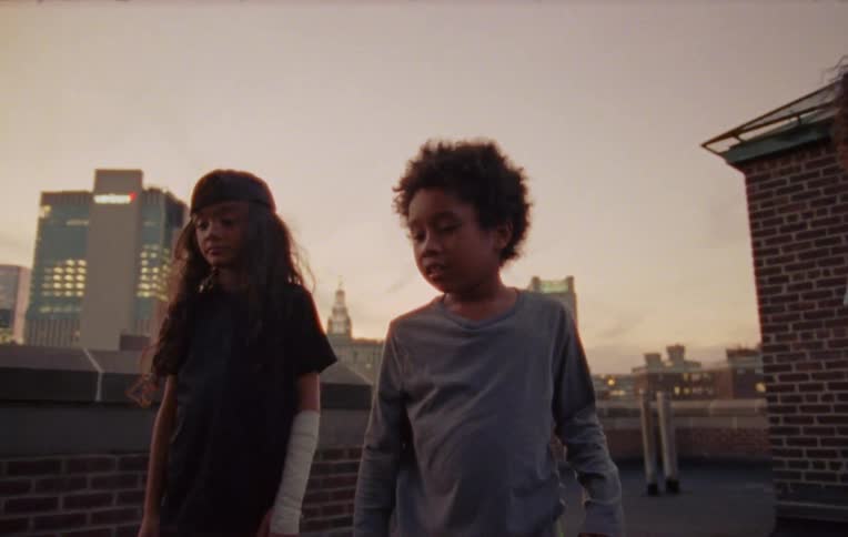 Three children on the terrace of a building when one of them throws an object and the friend beside gives a thumbsup signal