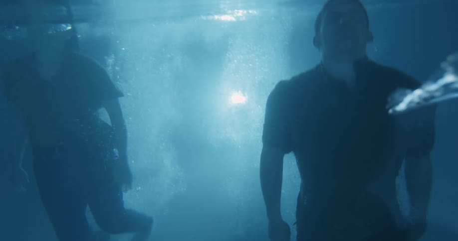 Two fully clothed people dive into a swimming pool at night