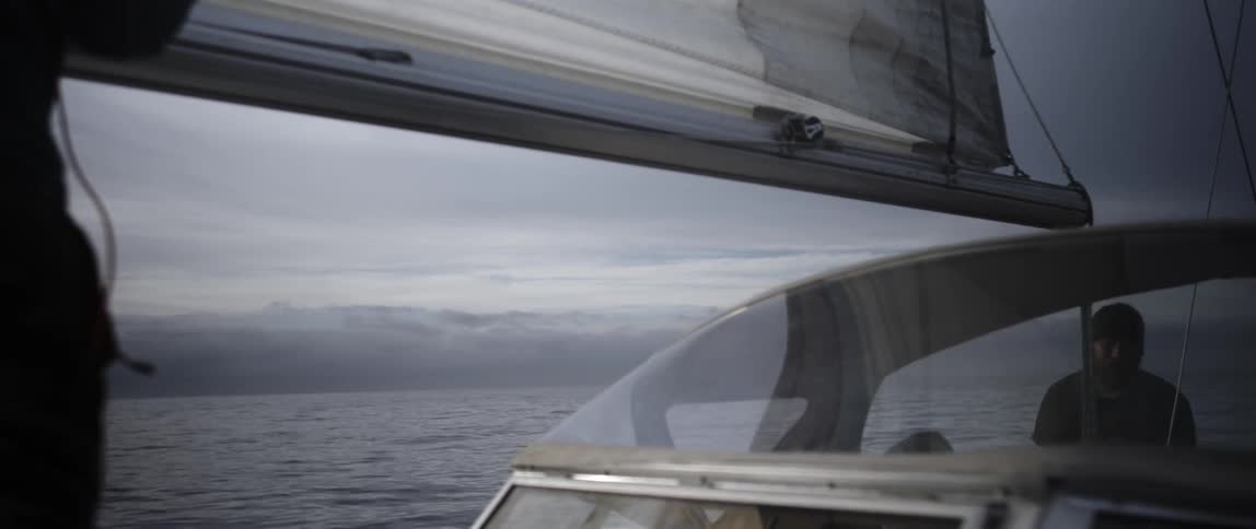 A boat sail turns and a man pulls the rope to bring it back